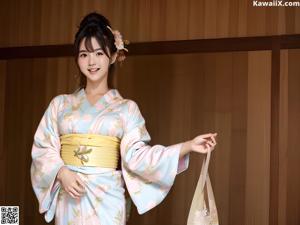 A woman in a blue kimono standing on a sidewalk.