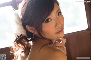 A naked asian woman sitting on a bed in front of a window.