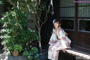 A naked asian woman sitting on a bed next to a window.