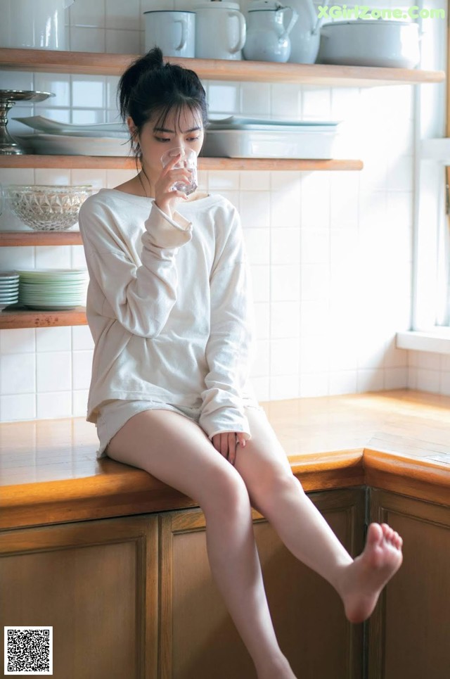 A woman sitting on a kitchen counter drinking water.