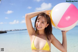 A woman in a yellow bikini sitting in the water.