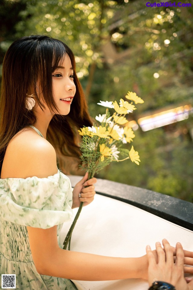 A woman in a green dress holding a bunch of flowers.