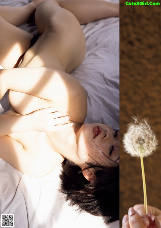 A naked woman laying on a bed next to a dandelion.