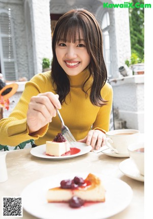 A woman in a yellow sweater and plaid skirt holding a camera.