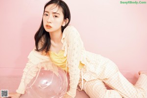 A woman sitting on a pink couch next to a pink wall.