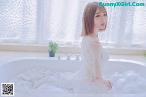 A woman in a white dress sitting in a bathtub.