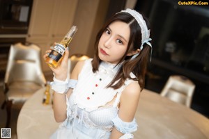 A woman sitting at a table with a bottle of beer.