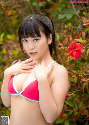 A woman in a red bathing suit smelling a red flower.