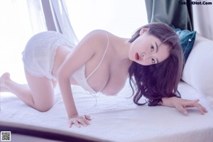 A woman in a white lingerie sitting on a bed.