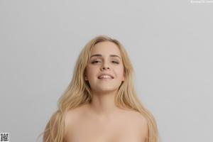 A young woman is posing naked on a black couch.