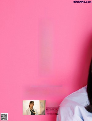 A woman in a blue shirt and gray skirt sitting on a pink background.