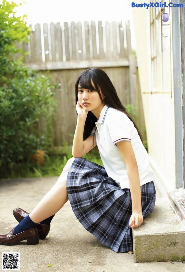A young woman in a school uniform sitting on a ledge.