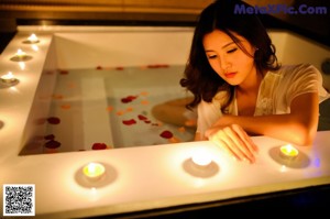 A woman sitting in a bathtub with candles in it.