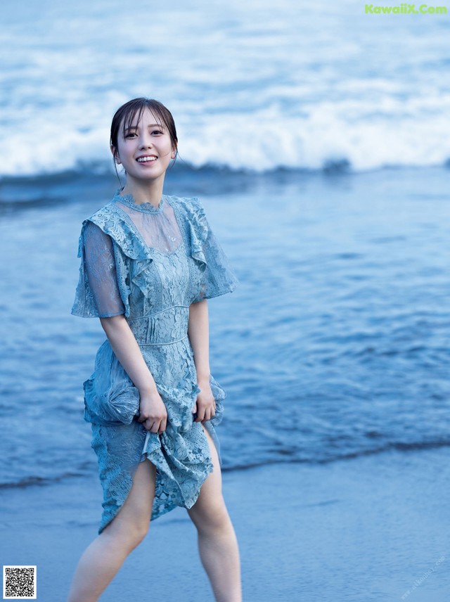 A woman in a blue dress standing on the beach.