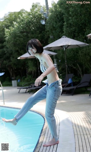 A woman in a bikini sitting on a stool by a pool.