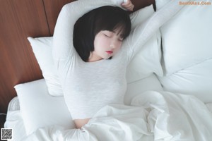 A woman in a white top and panties sitting on a bed.