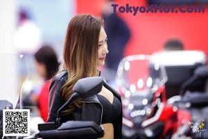 A woman in a leather jacket sitting on a red motorcycle.
