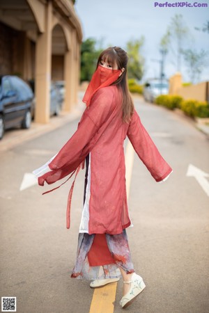 A woman in a red robe leaning against a wall.